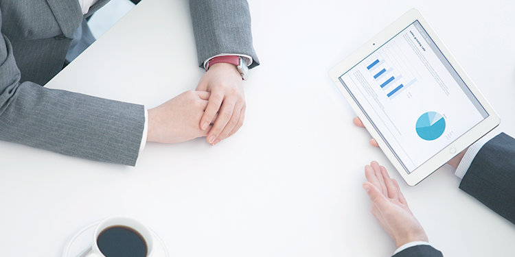 两人坐在一张白色的桌子旁，其中一人用平板电脑显示数据并提出建议。