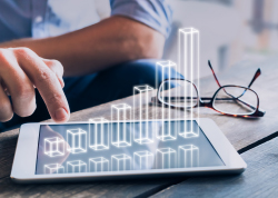 一人与数字平板电脑互动，数字平板电脑显示上升条形图，旁边的桌面上放着一副眼镜。